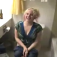 A blonde girl is observed peeing while sitting on a toilet while her friends wait in the other room.
